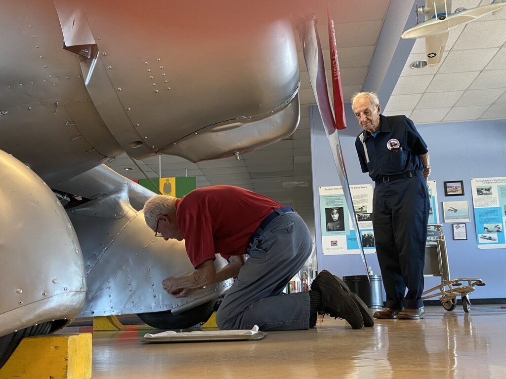 An image of Nelson Faso looking on as Jim Birke works on an airplane